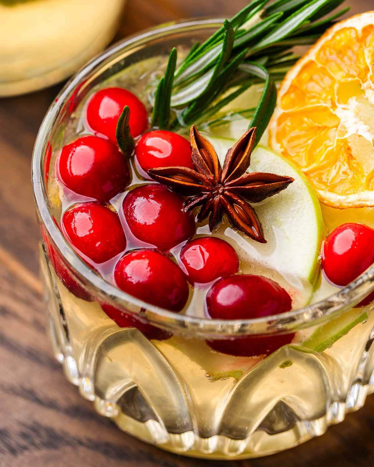 Sangria with cranberries, star anise, and rosemary in small glass.