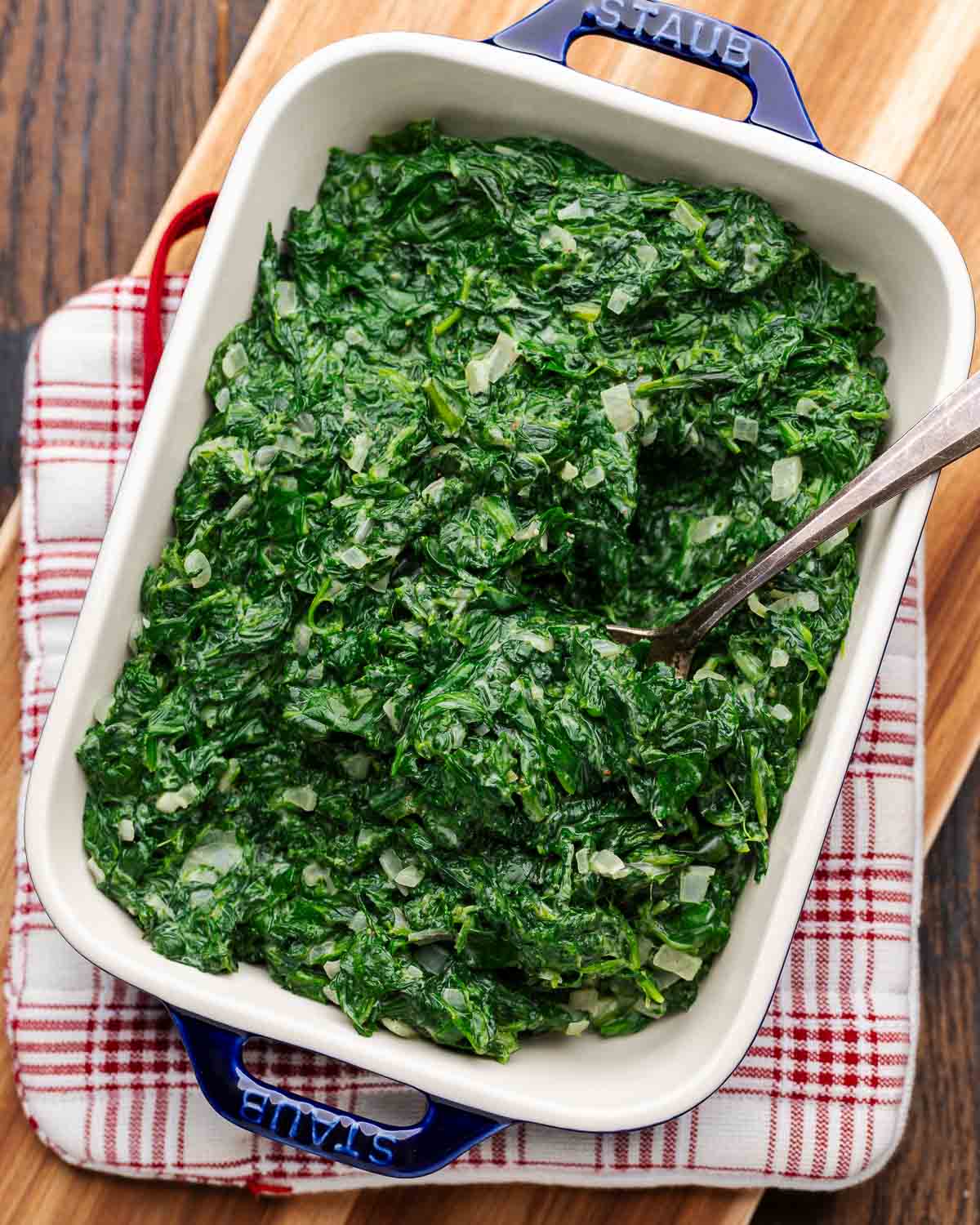 Creamed spinach in platter on top of red and white heat pad and wooden board.