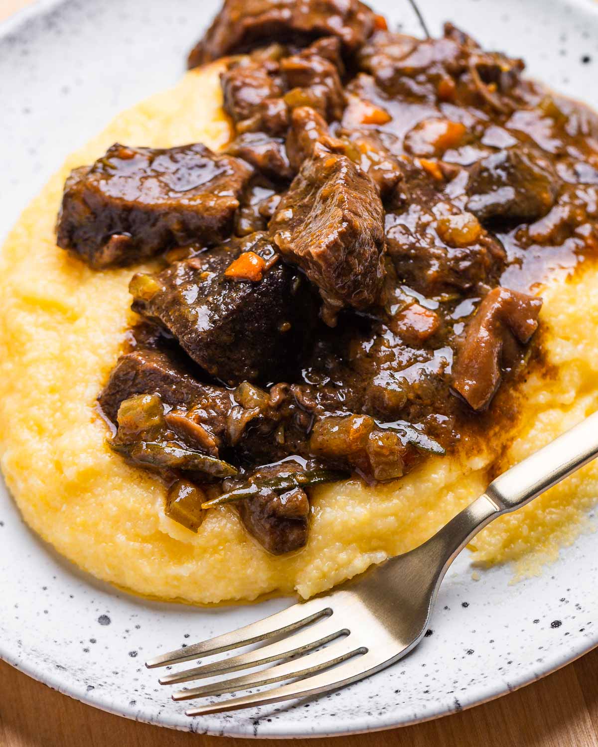 Creamy polenta topped with beef stew in white plate.