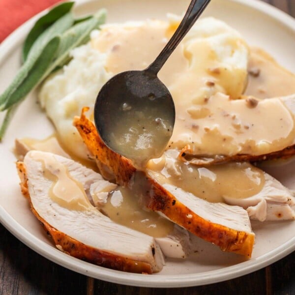 Featured image of giblet gravy poured over turkey and mashed potatoes in tan plate.