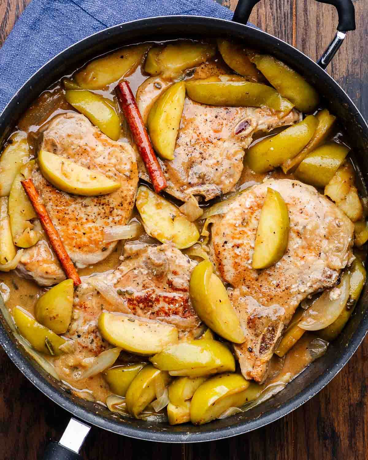 Overhead shot of large black pan with pork chops and apples.