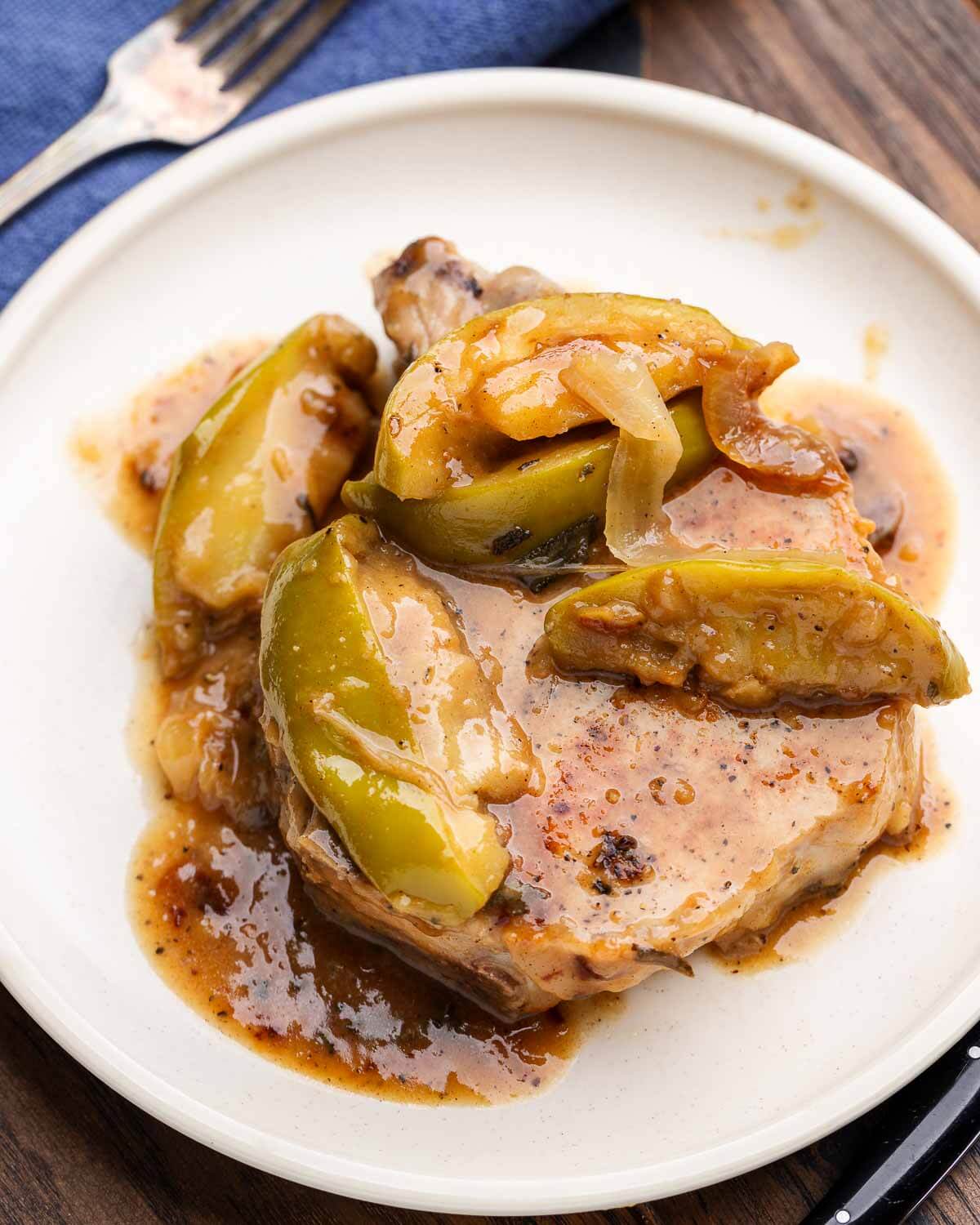 White plate with pork chop and apples on table.