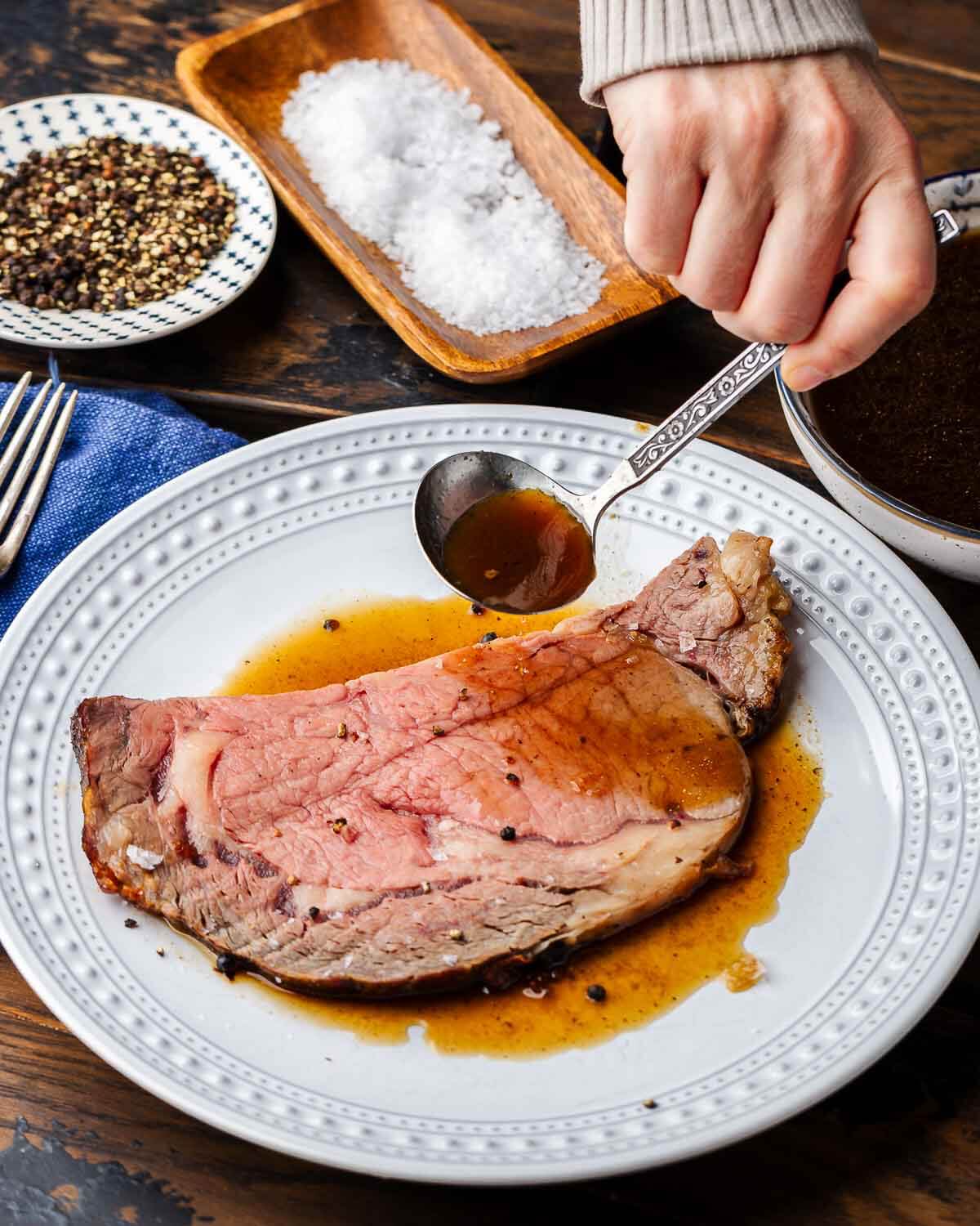 Hands ladling au jus onto slice of prime rib.