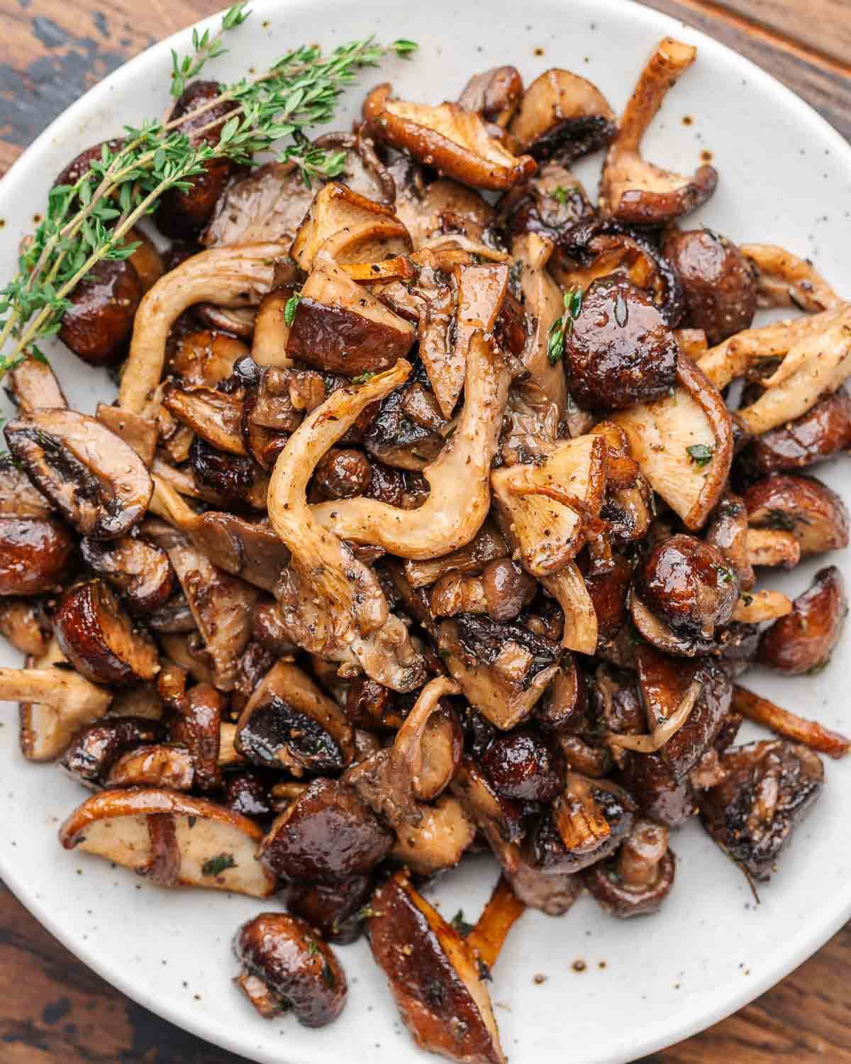 Roasted mushrooms with thyme garnish in white plate.