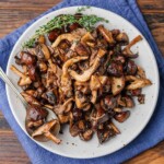 Featured image of roasted mushrooms with thyme garnish in white plate on blue napkin.