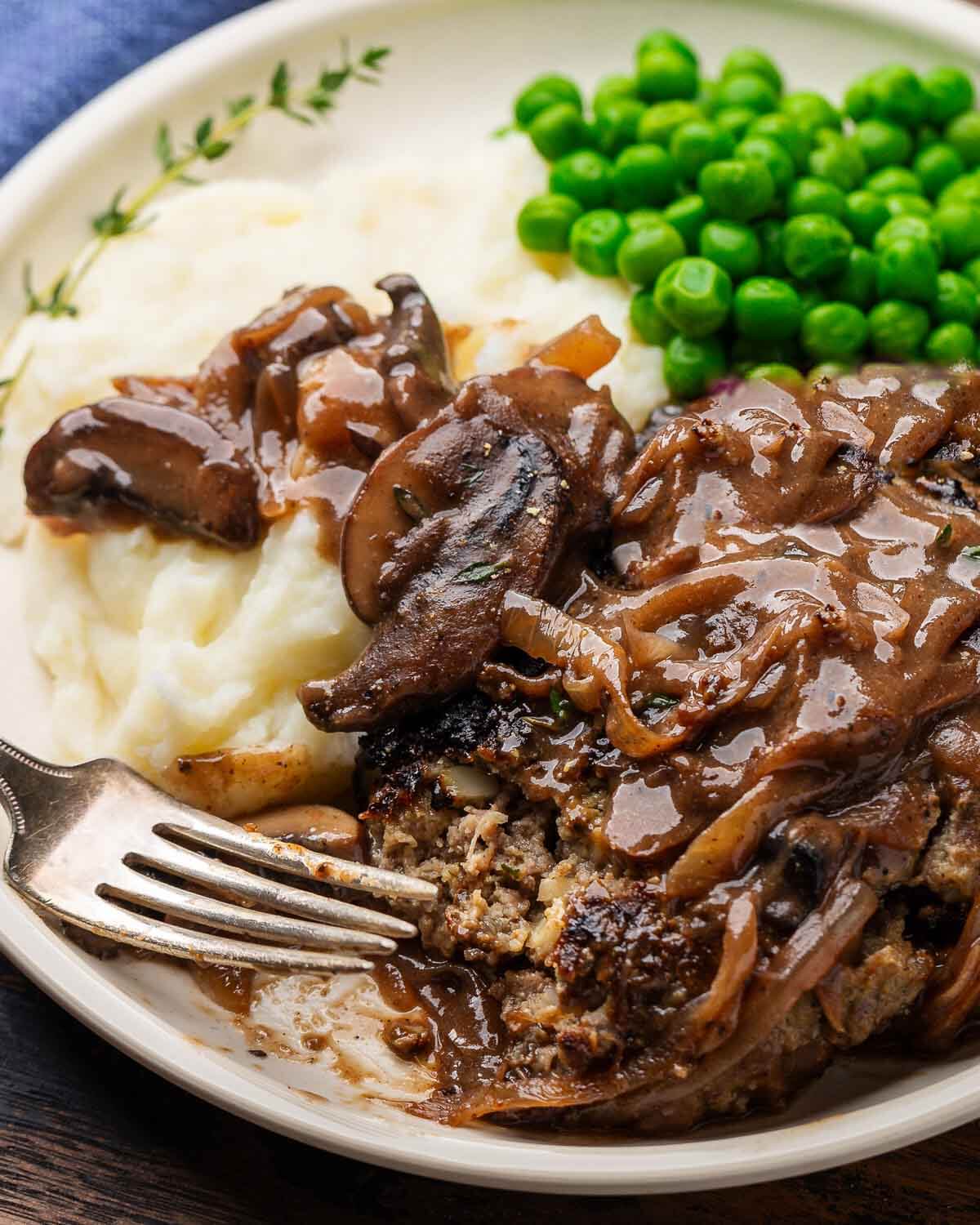 Plate with cut salisbury steak, peas, and mashed potatoes.