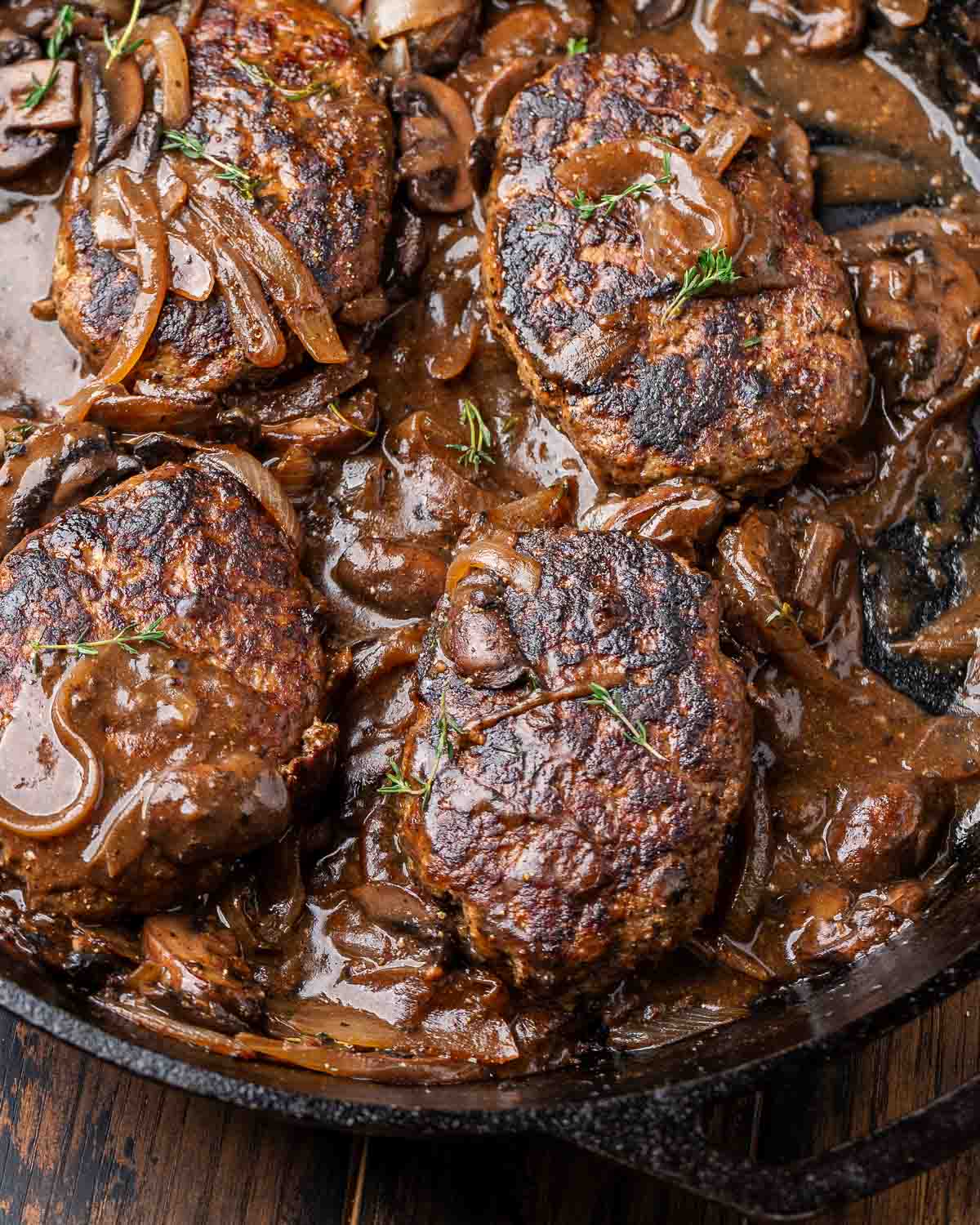 Cast iron pan with 4 salisbury steaks topped with mushroom gravy.