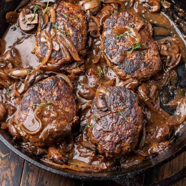 Featured image of salisbury steaks and mushroom gravy in cast iron pan with thyme garnish.
