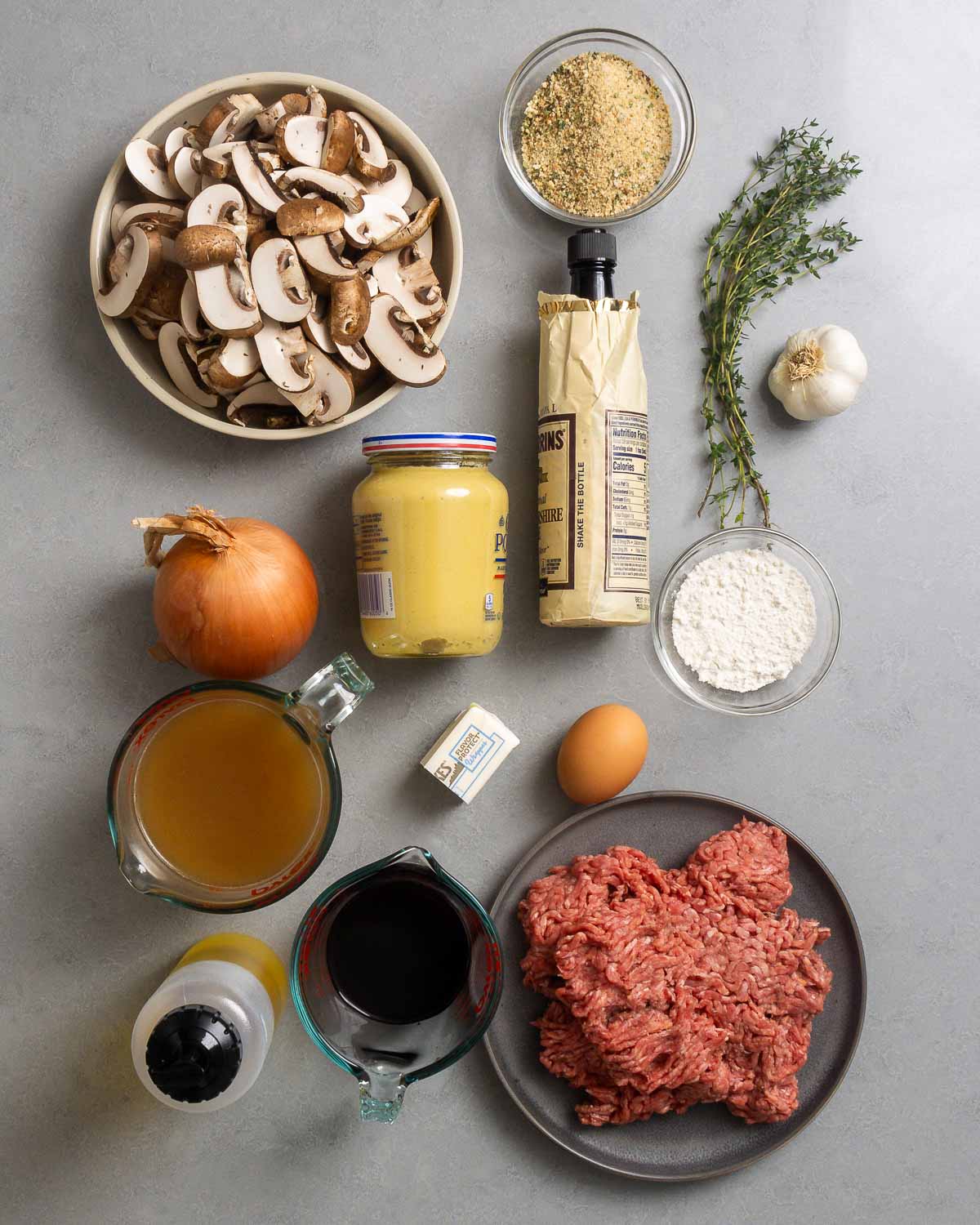 Ingredients shown: mushrooms, breadcrumbs, worcestershire sauce, thyme, garlic, Dijon mustard, onion, flour, beef stock, butter, egg, olive oil, red wine, and ground 80/20 chuck.