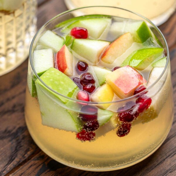 White wine sangria feature image of small glass with apples, pear, and pomegranate seeds.