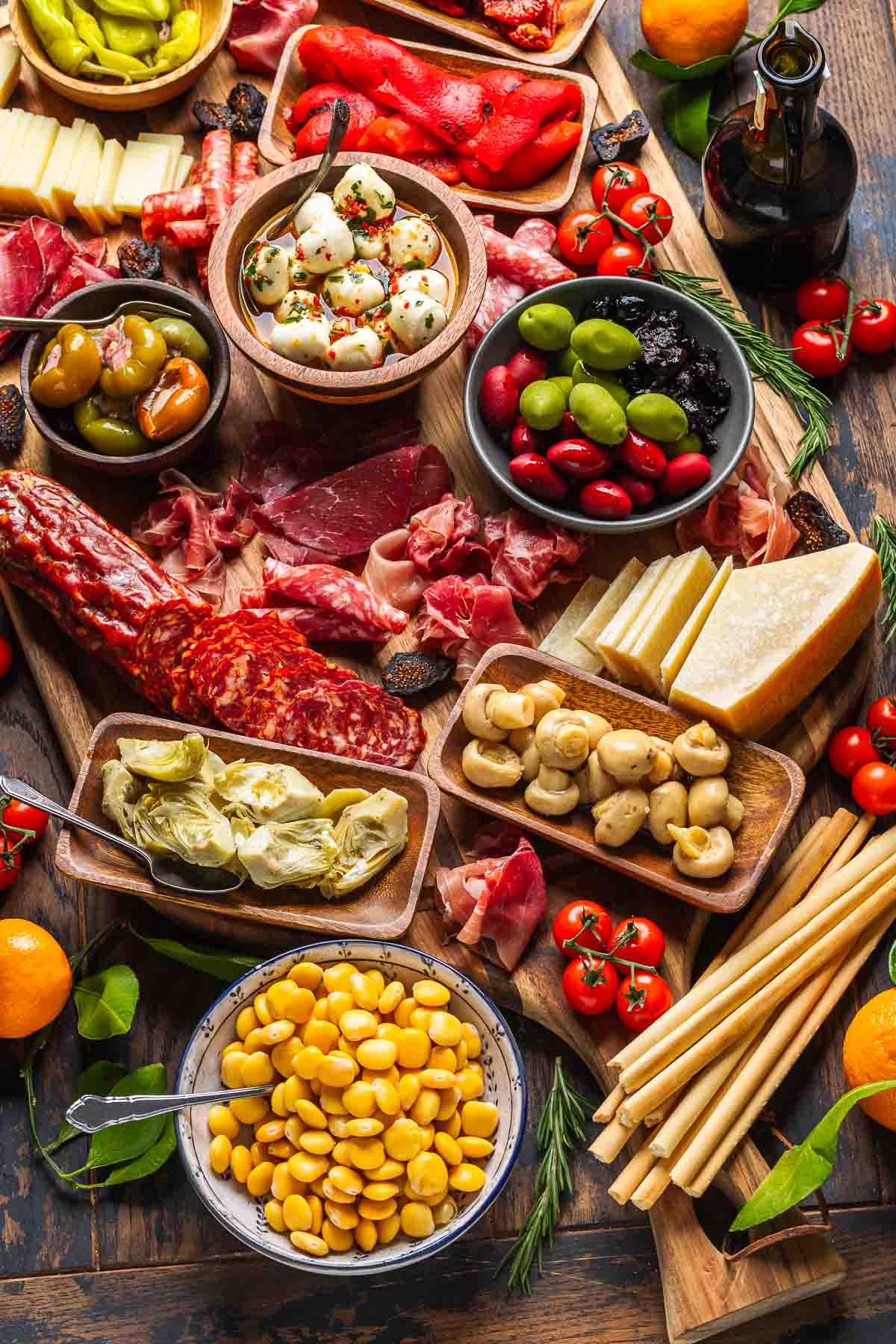 Closeup shot of antipasto platter with meats, cheeses, olives, pickled vegetables, lupini beans, and breadsticks.