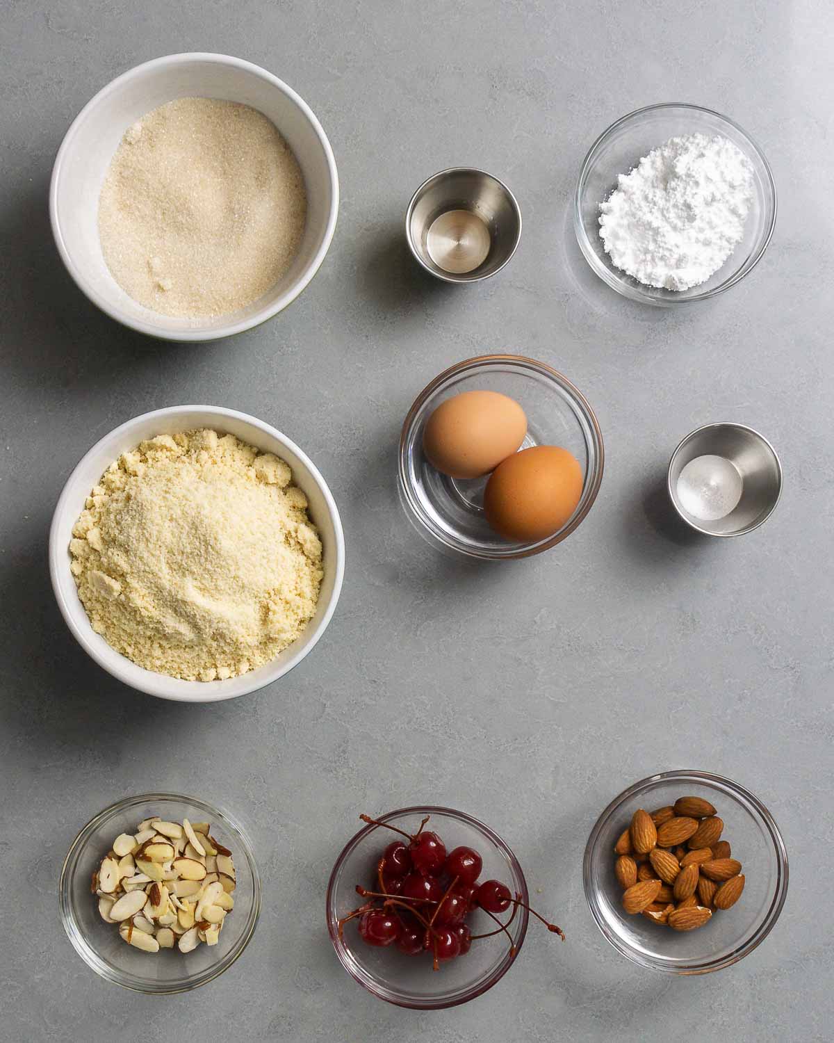 Ingredients shown: sugar, almond extract, powdered sugar, almond flour, eggs, salt, almonds, and cherries.