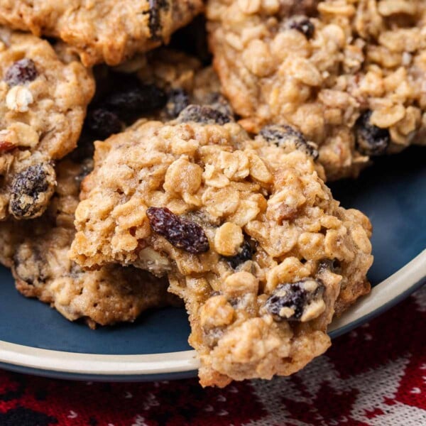 Oatmeal raisin pecan cookies on blue plate with one cookie having a bite taken out of it.