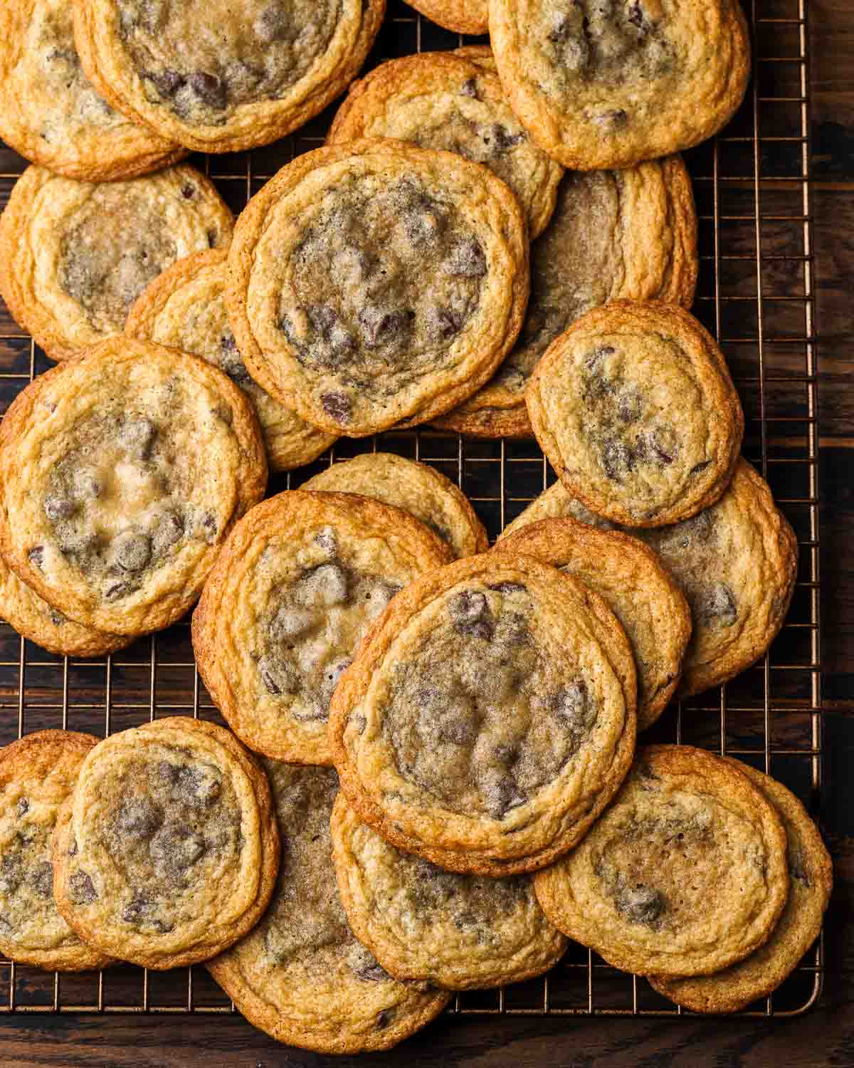 Large amount of pan banged chocolate chip cookies on wire rack.