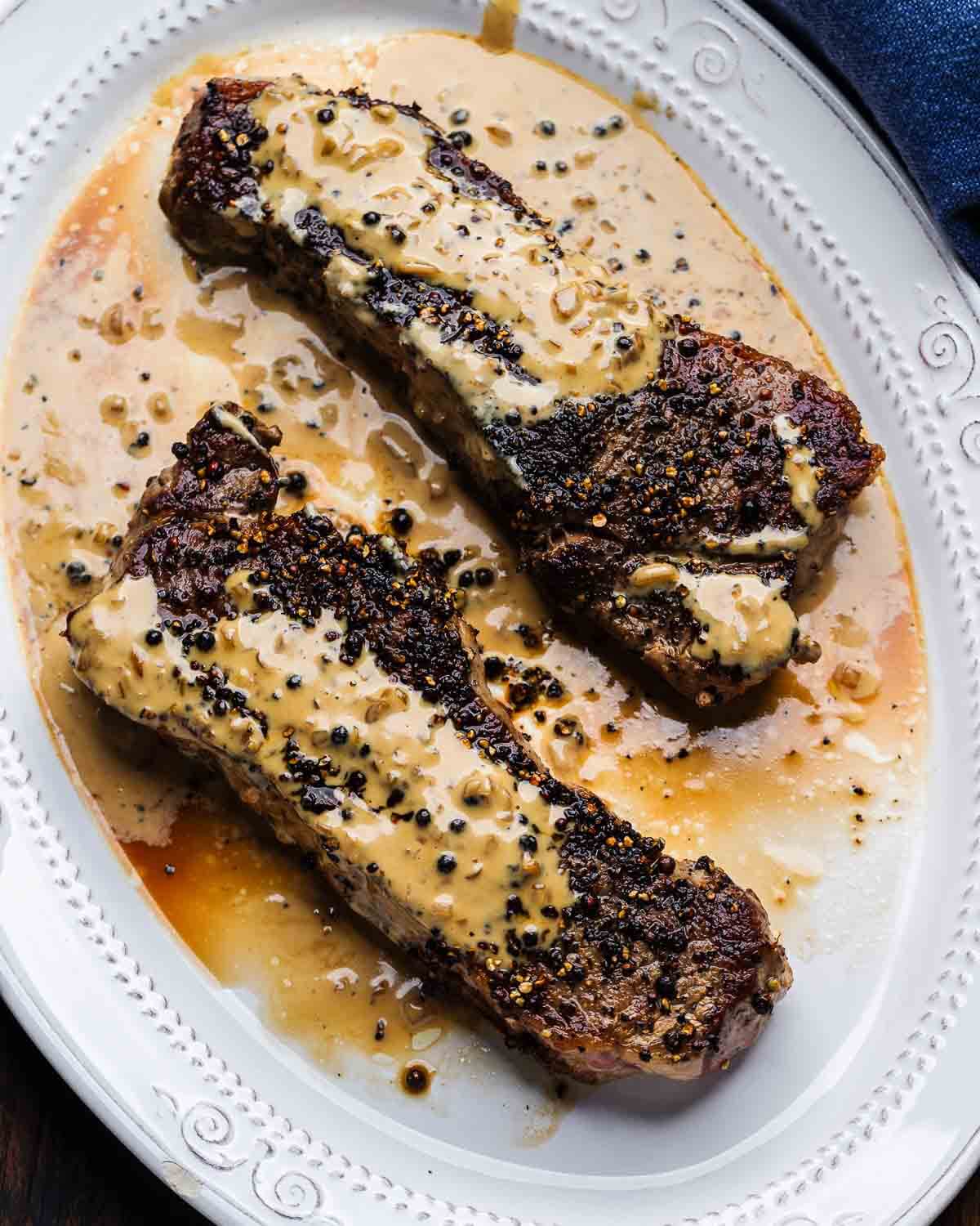 Steak au poivre in white platter with blue napkin.