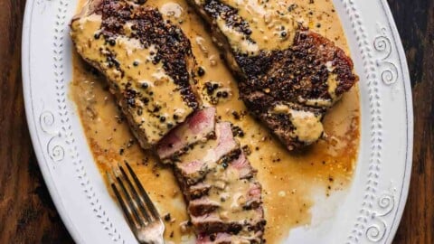 Steak au poivre in white platter white on table.