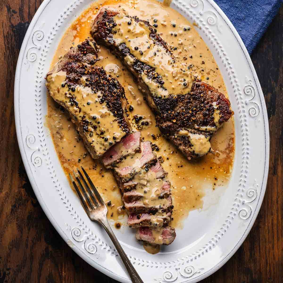 Steak au poivre in white platter on table.