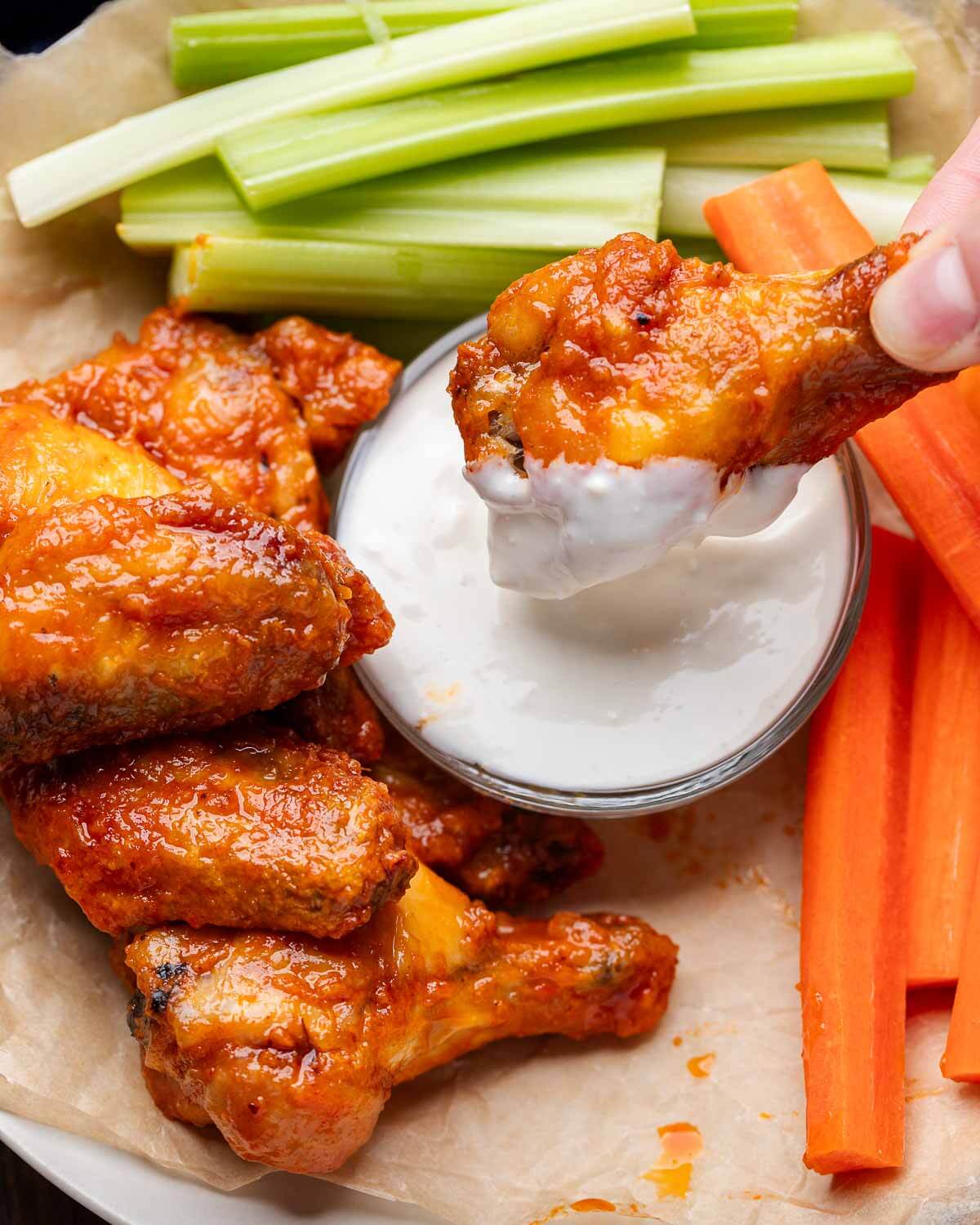 Hand dipping buffalo wing into blue cheese dressing.