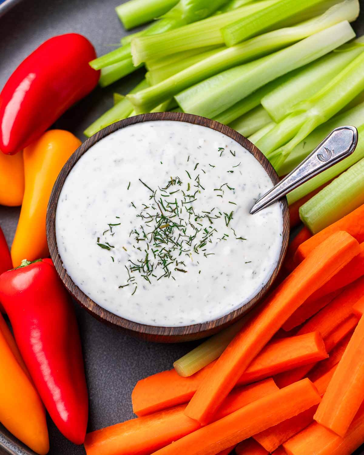 Grey plate with bowl of ranch dressing and cut vegetables.