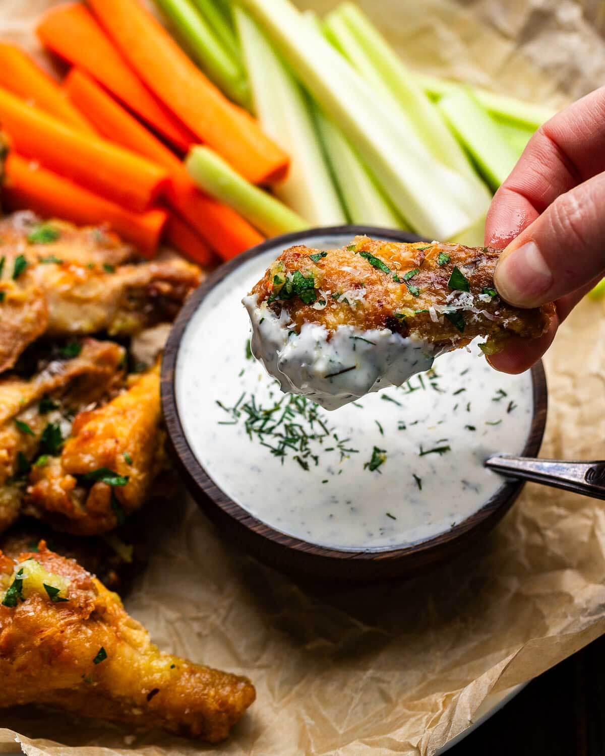 Hands dipping chicken wing into ranch dressing.