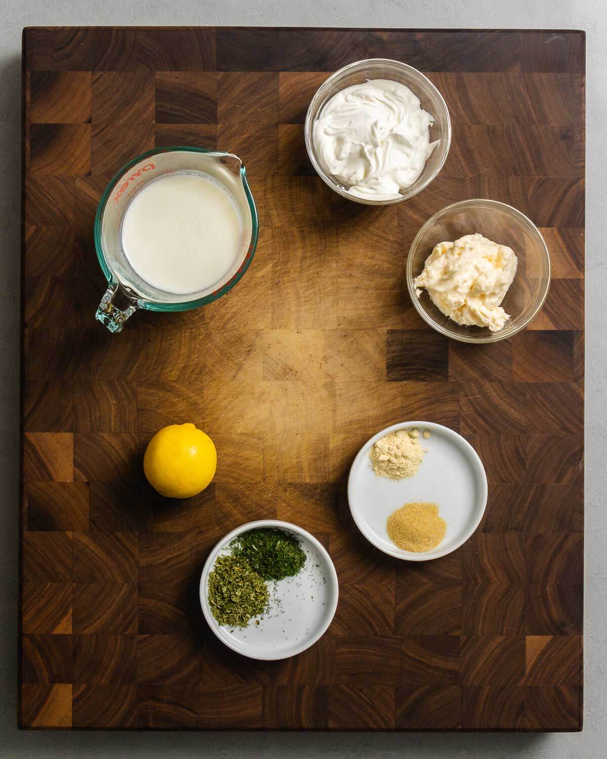 Ingredients shown: buttermilk, mayonnaise, sour cream, lemon, granulated garlic, onion powder, dried parsley, and dried dill.