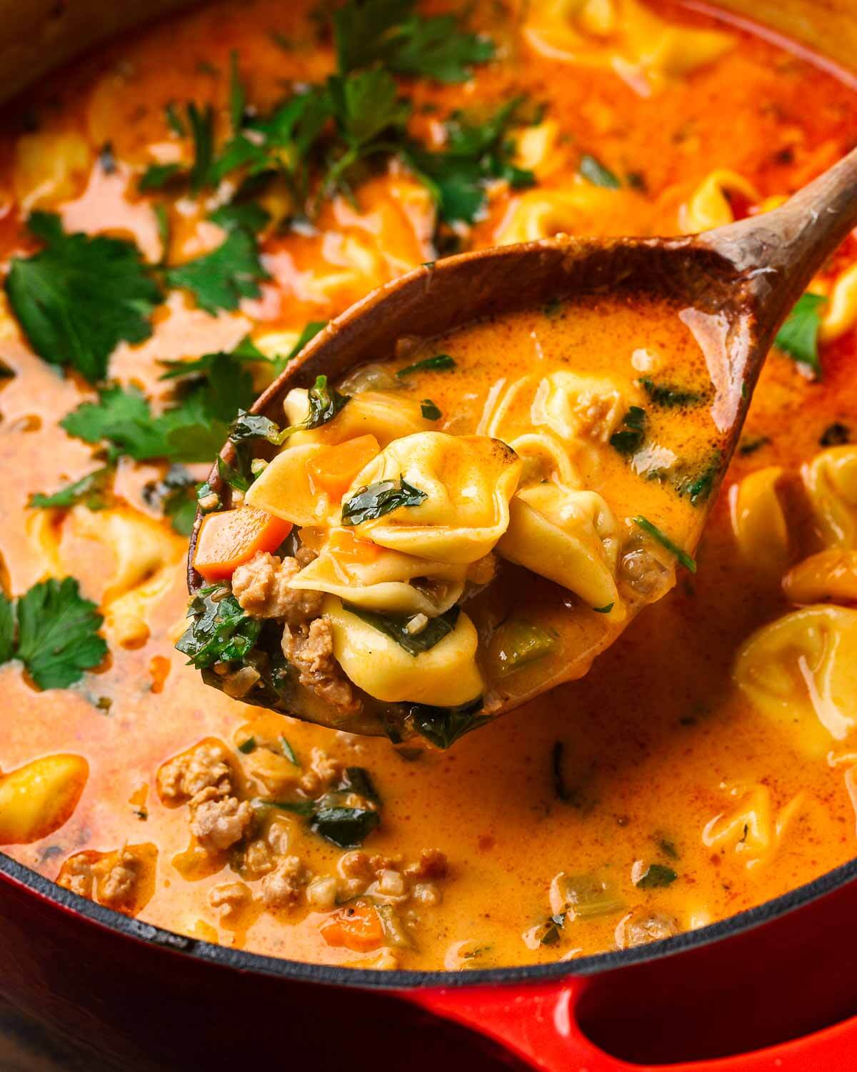 Large pot of soup with wooden ladle holding tortellini.