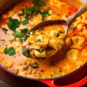 Creamy sausage tortellini in large Dutch oven with wooden ladle for featured image.