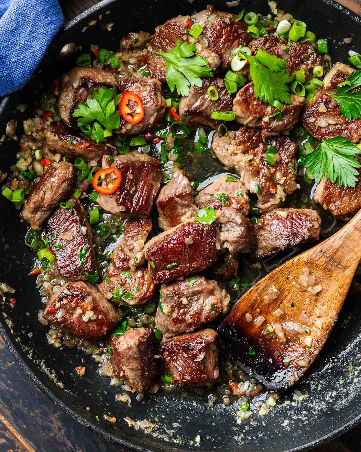 Large black pan with seared steak bites topped with parsley and green onions.