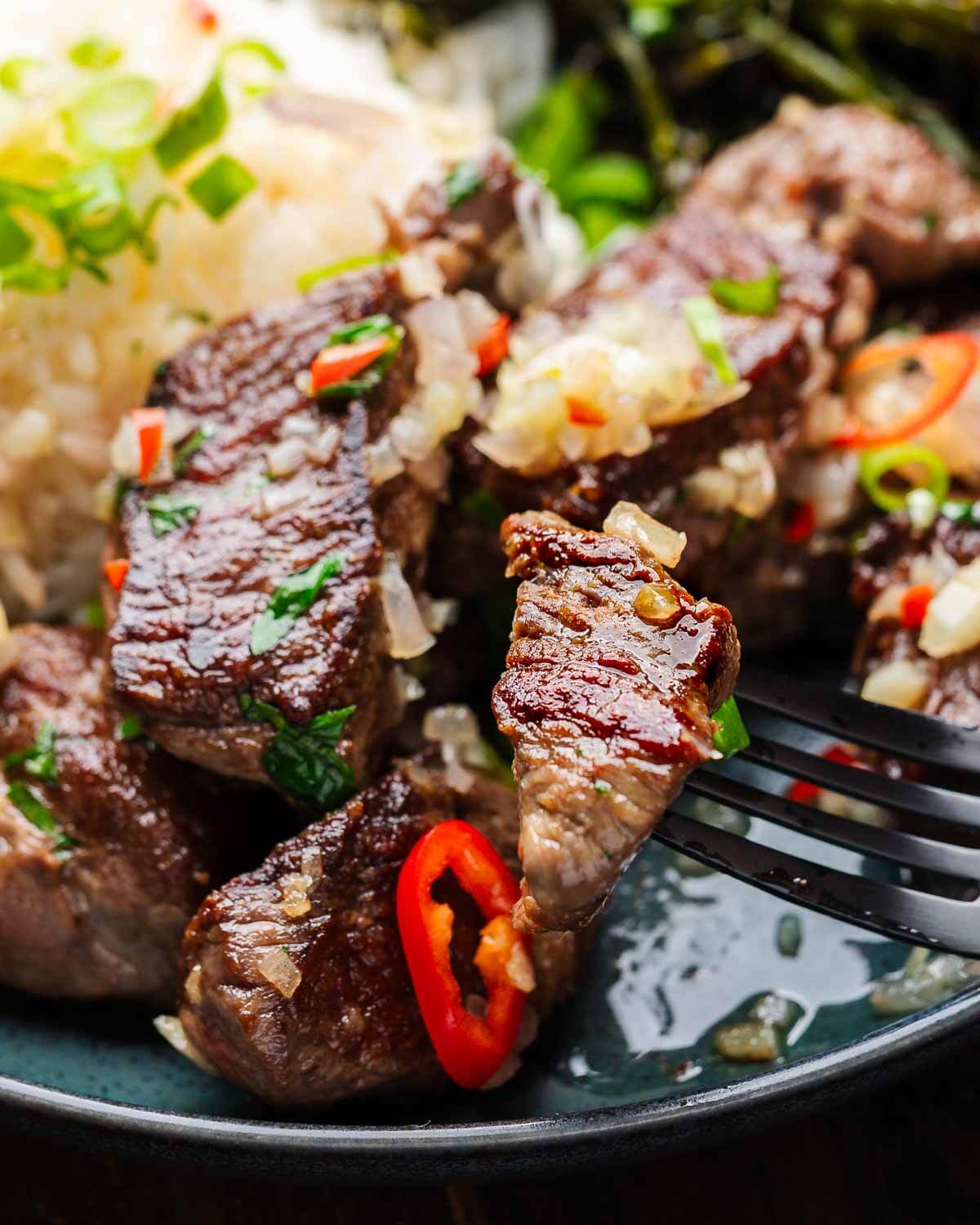 Fork holding one garlic butter steak bite above plate.