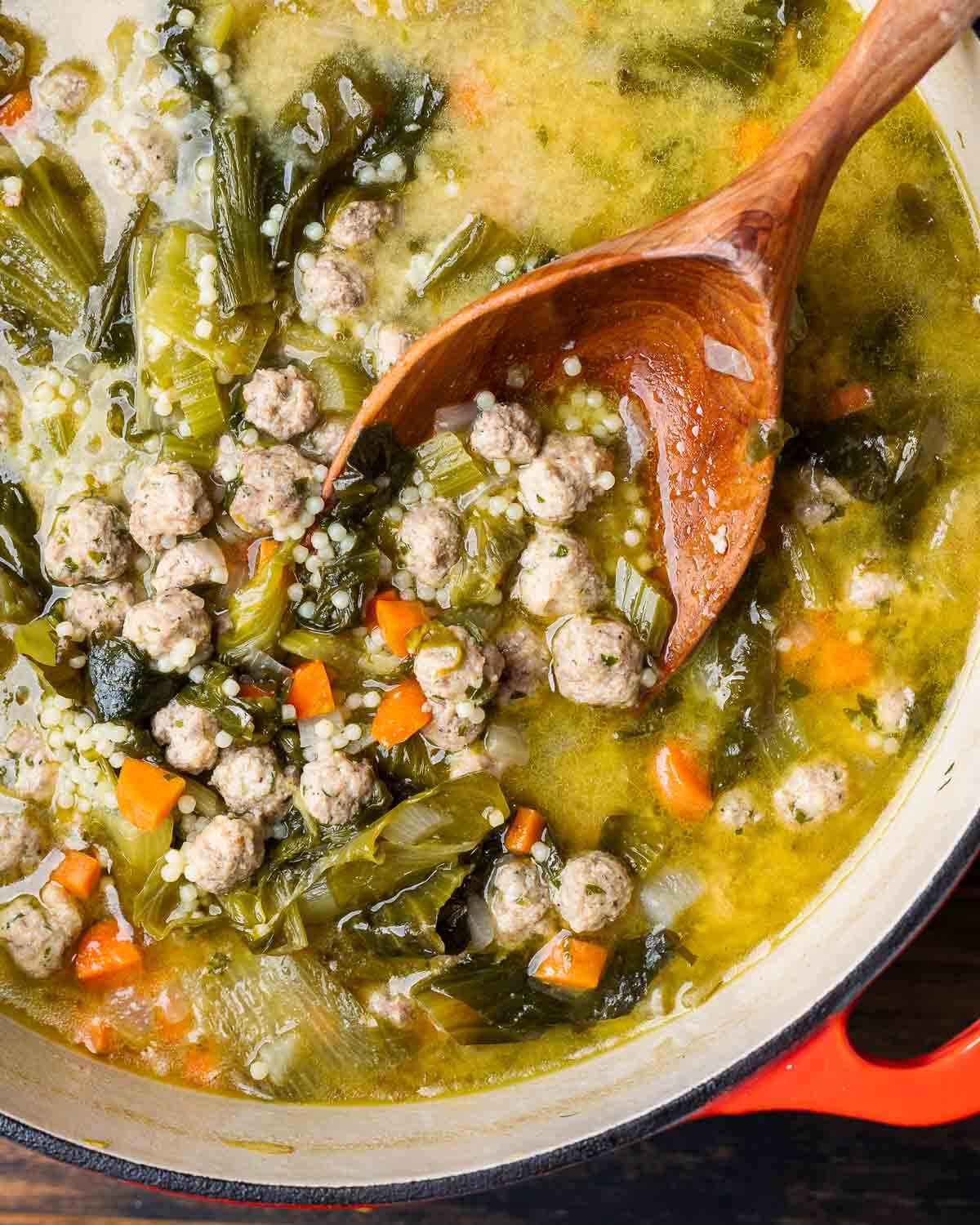 Large pot of Italian wedding soup with wooden ladle scooping out the meatballs.
