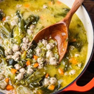 Italian wedding soup in large pot with wooden ladle for featured image.