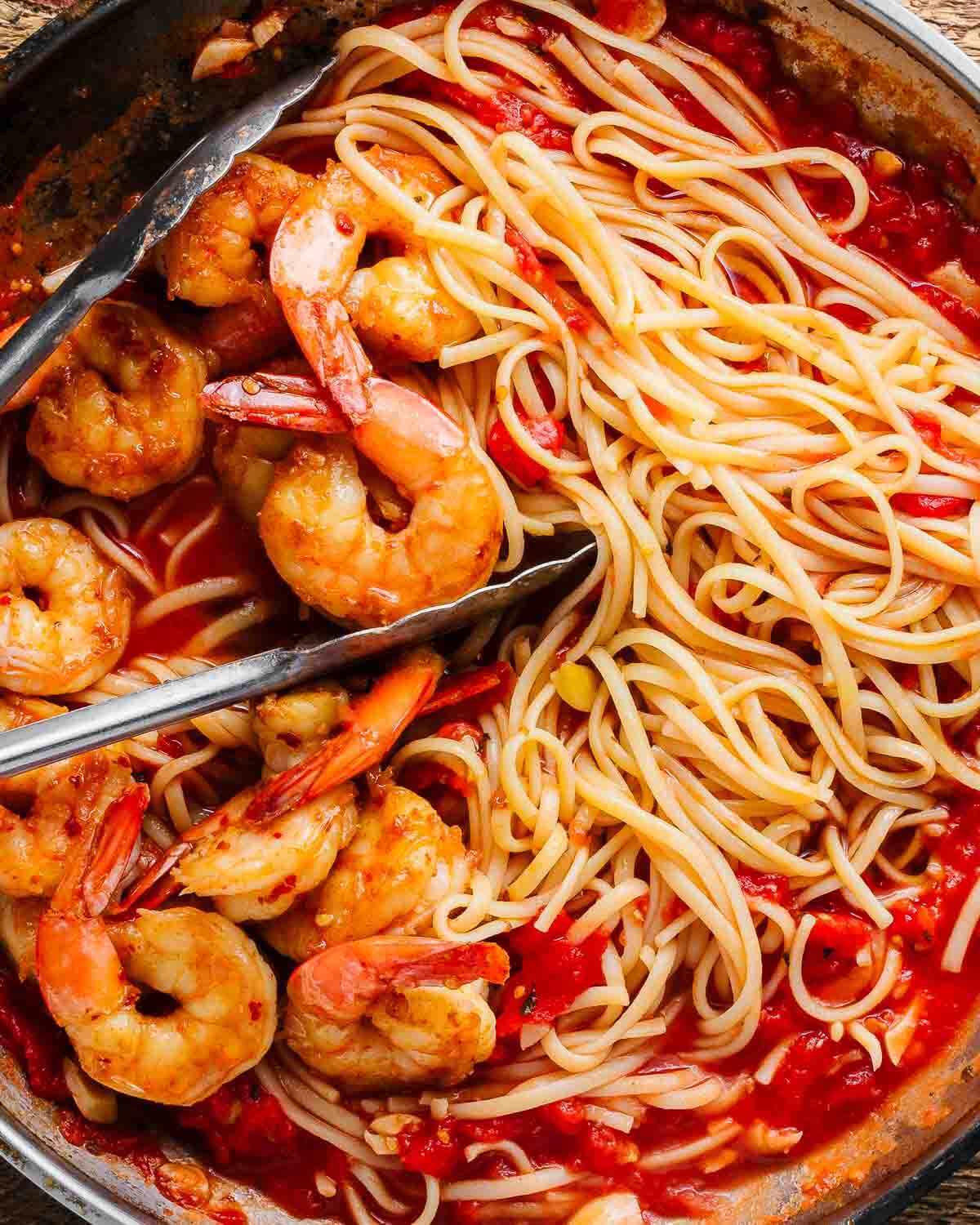 Shrimp fra diavolo in pan with tongs.