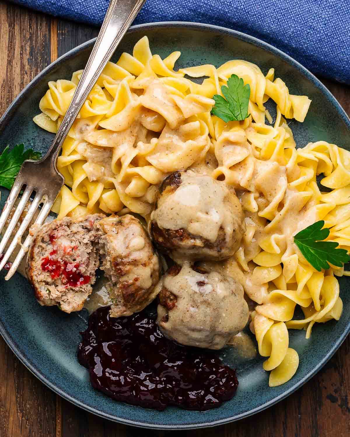 Swedish meatballs in grey plate over egg noodles with lingonberry jam.
