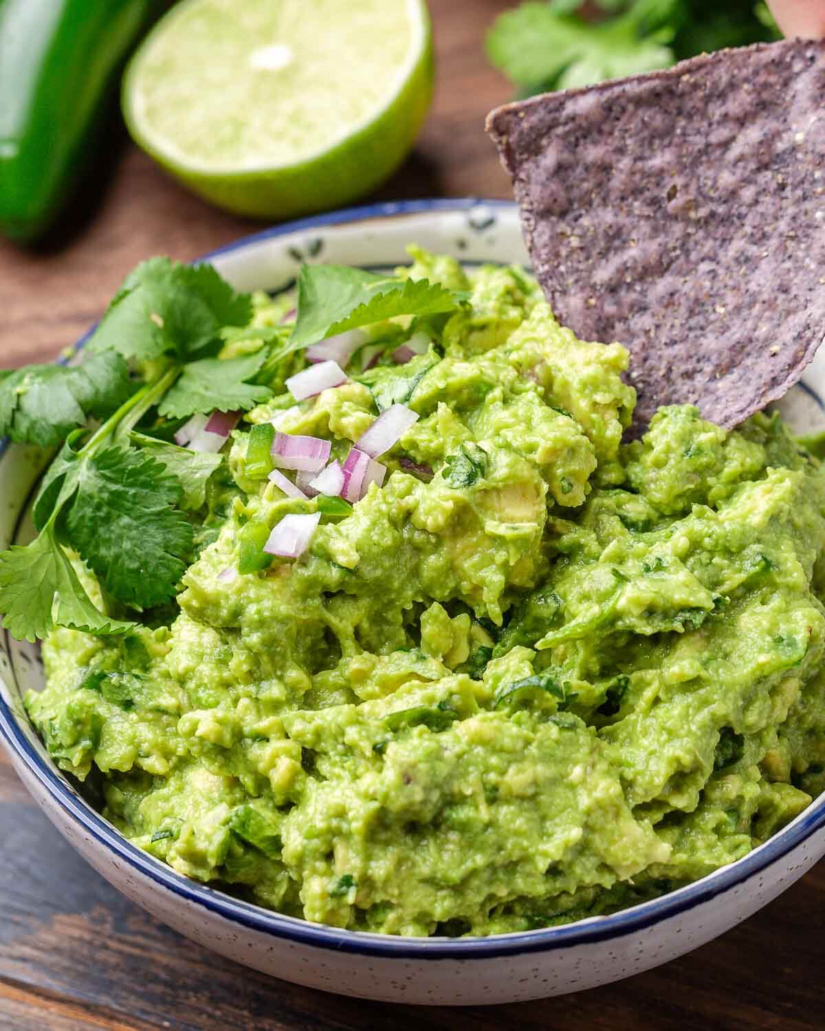 Blue corn chip dipped into bowl of guacamole.