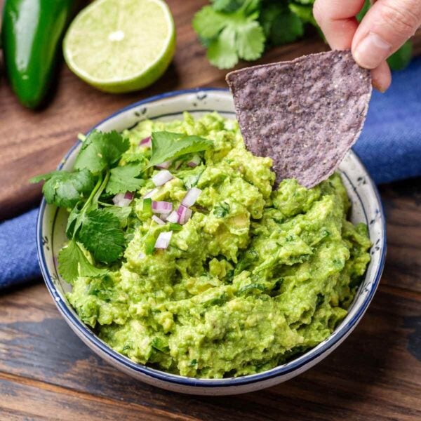 Blue corn chip dipped into bowl of guacamole for featured image.