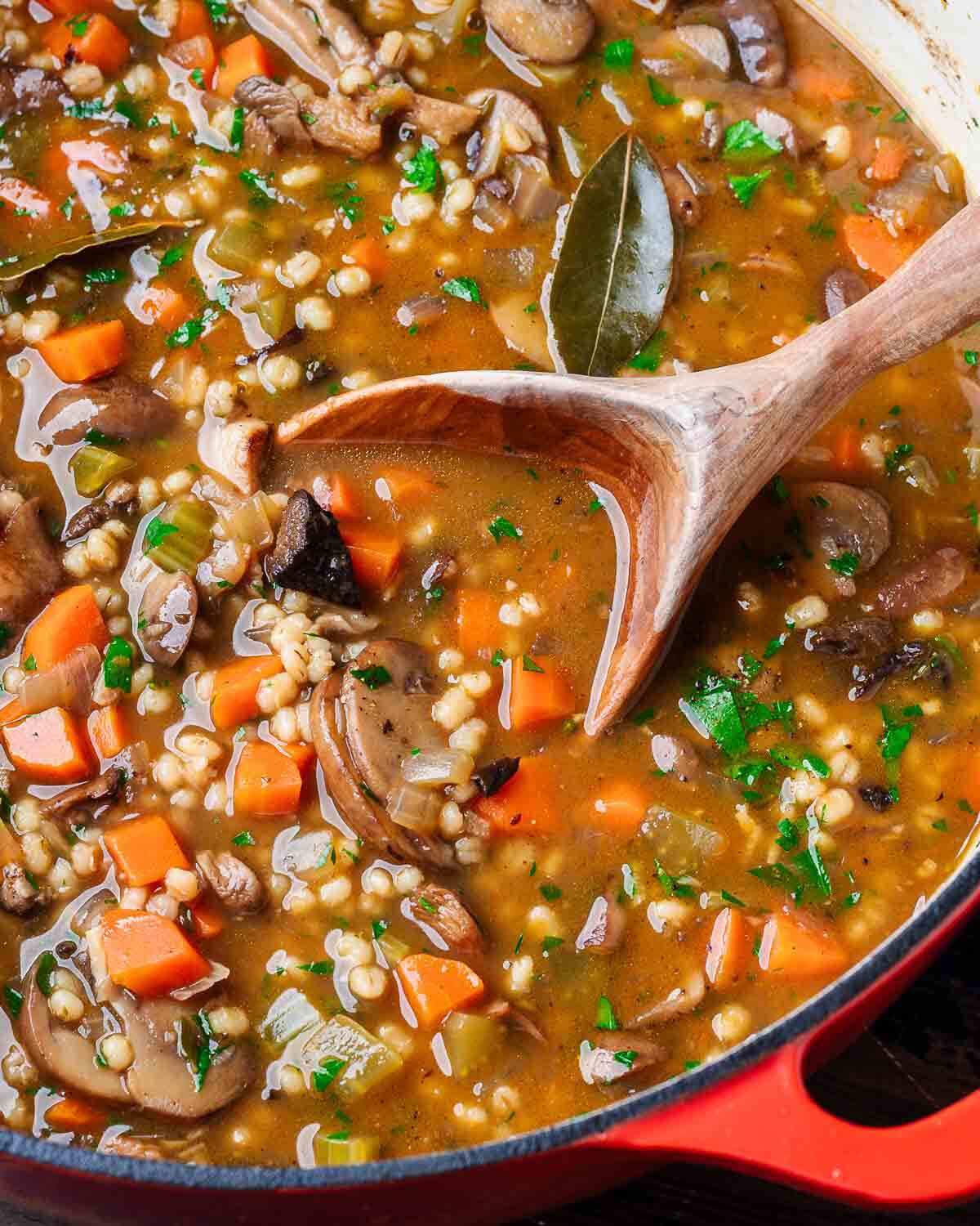 Large pot of mushroom barley soup with wooden ladle.