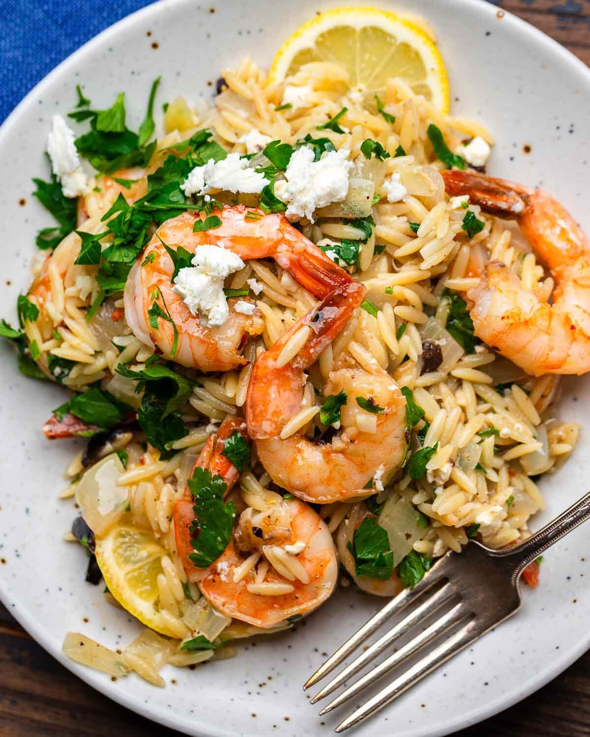 White plate with orzo topped with shrimp and parsley.