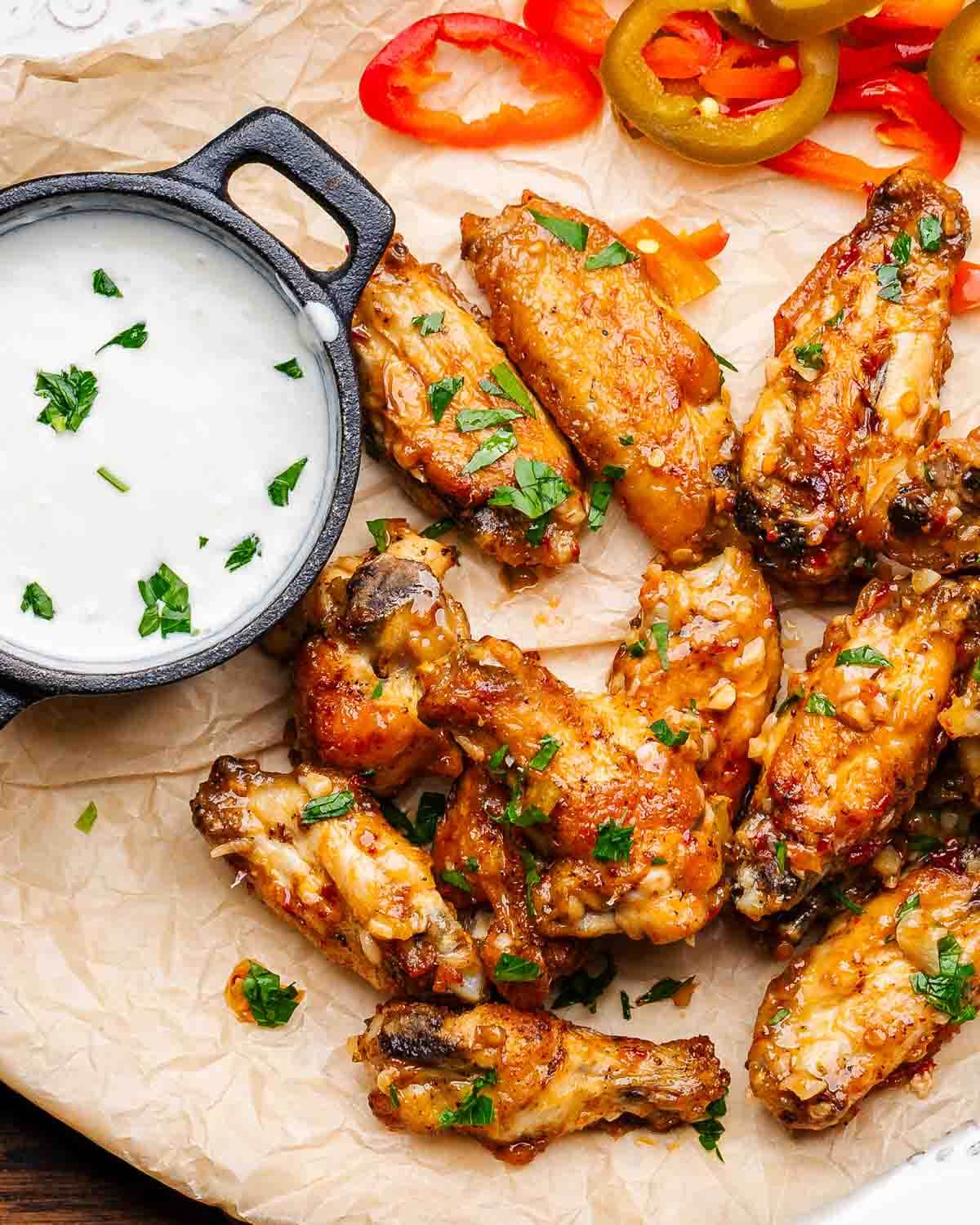 Scarpariello wings on parchment paper lined plate with blue cheese dressing and sliced cherry peppers.