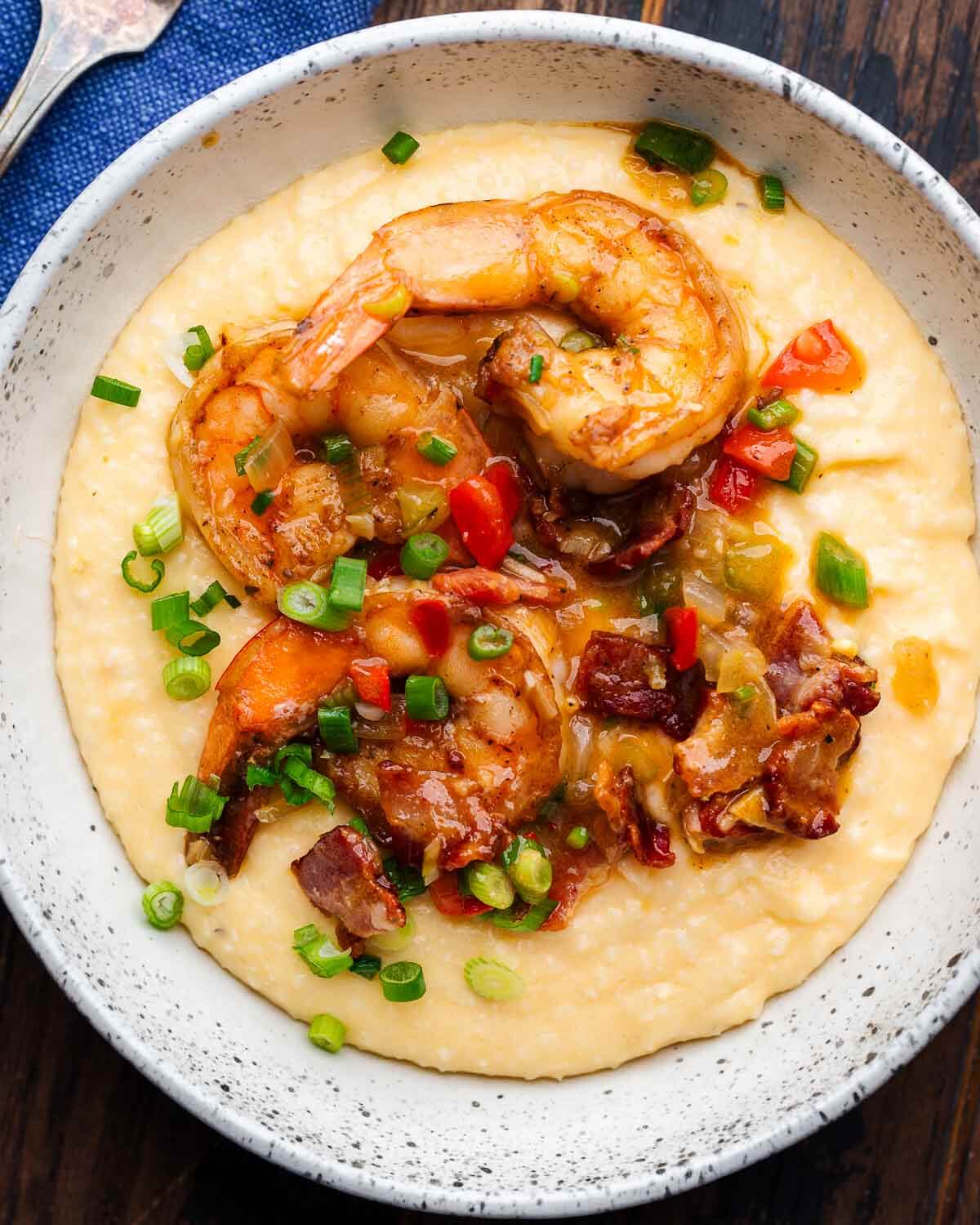 White bowl with shrimp and grits topped with bacon and green onions.
