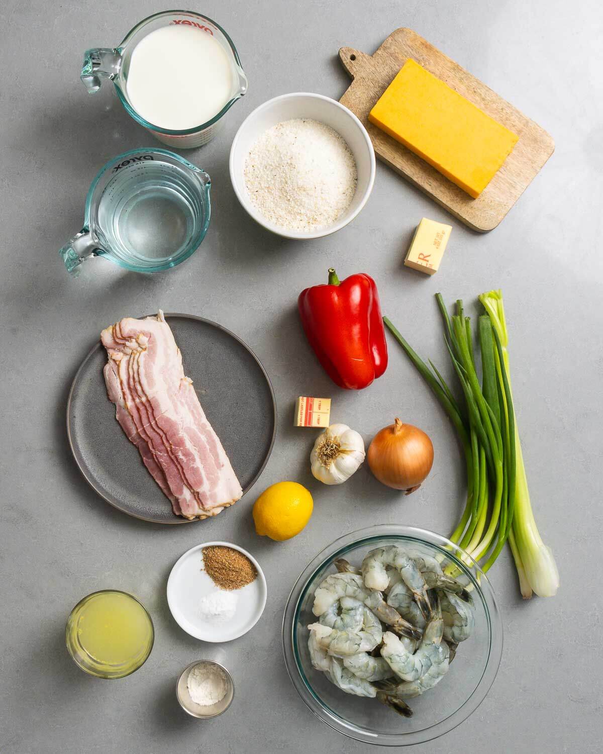 Ingredients shown: milk, water, grits, cheddar cheese, butter, bacon, bell pepper, garlic, onion, green onions, celery, chicken stock, spices, lemon, and shrimp.