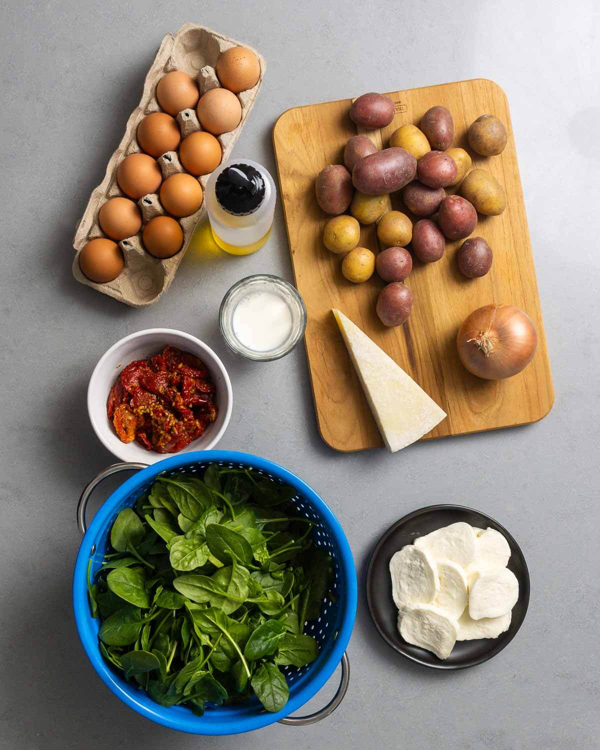 Ingredients shown: eggs, olive oil, milk, potatoes, onion, sun-dried tomatoes, spinach, Pecorino Romano, and sliced fresh mozzarella cheese.