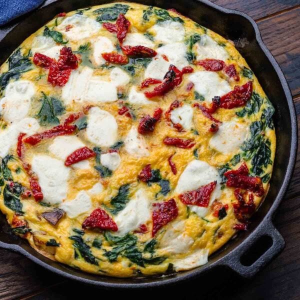 Sun dried tomato frittata in cast iron pan on wooden board for featured image.