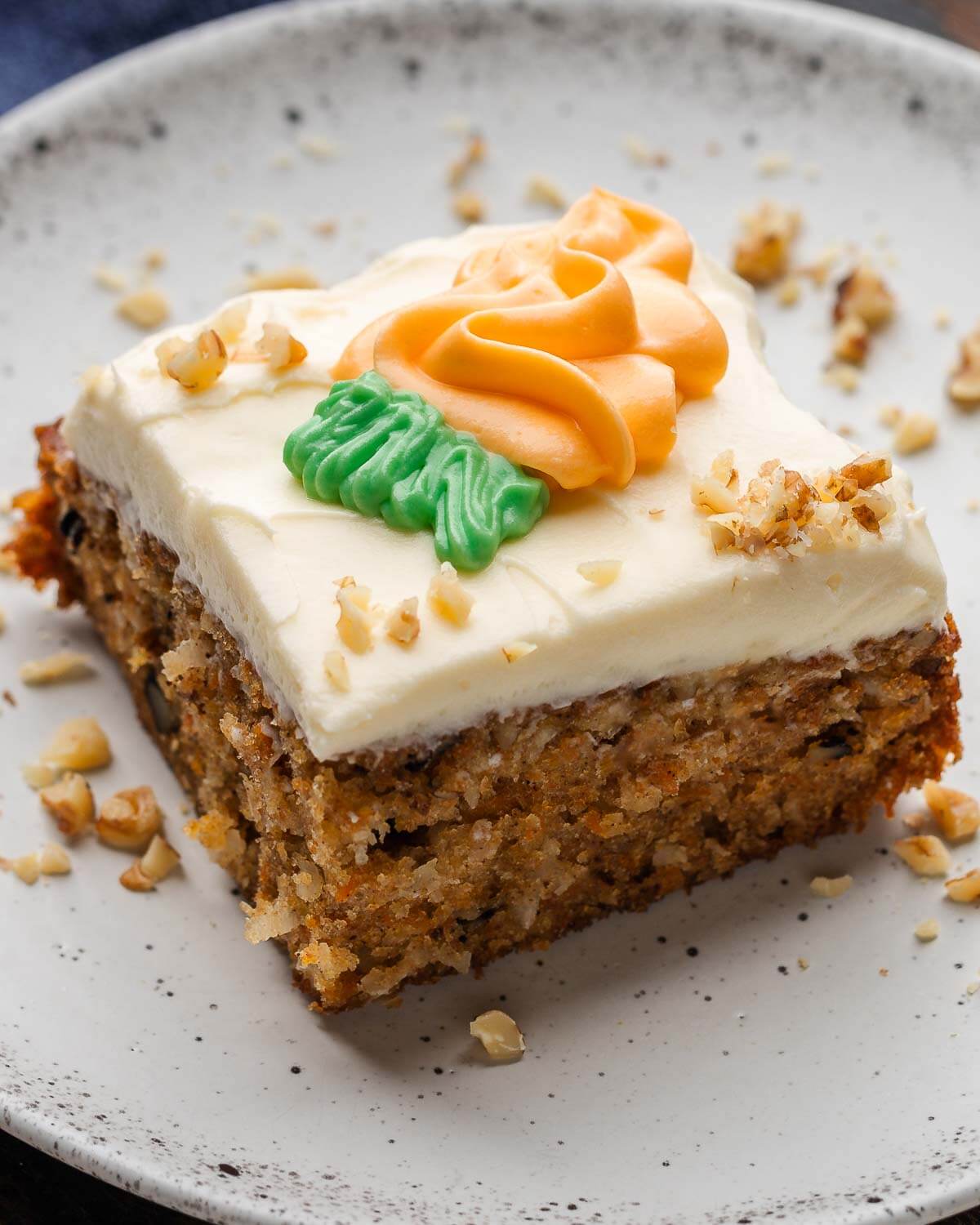 Carrot cake in white plate with sprinkled walnuts around the edges.