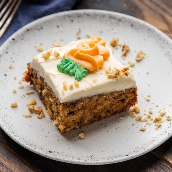 Carrot cake in white plate with sprinkled walnuts around the edges.