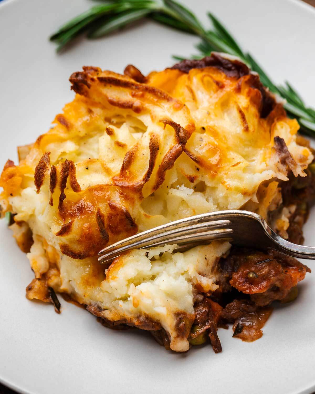 Fork scooping a piece of cottage pie in white plate.