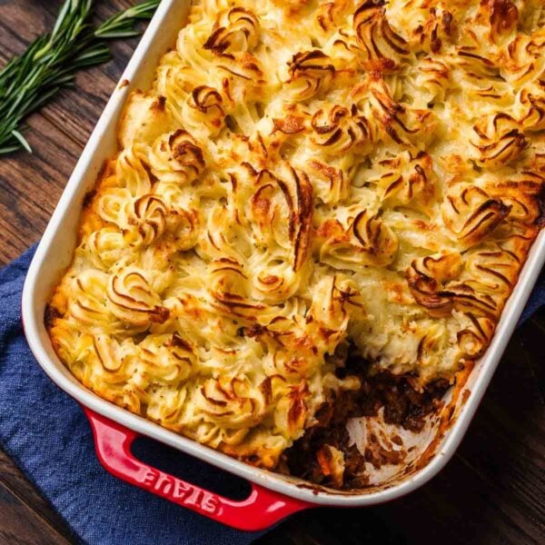 Cottage pie in red baking dish with piece removed.