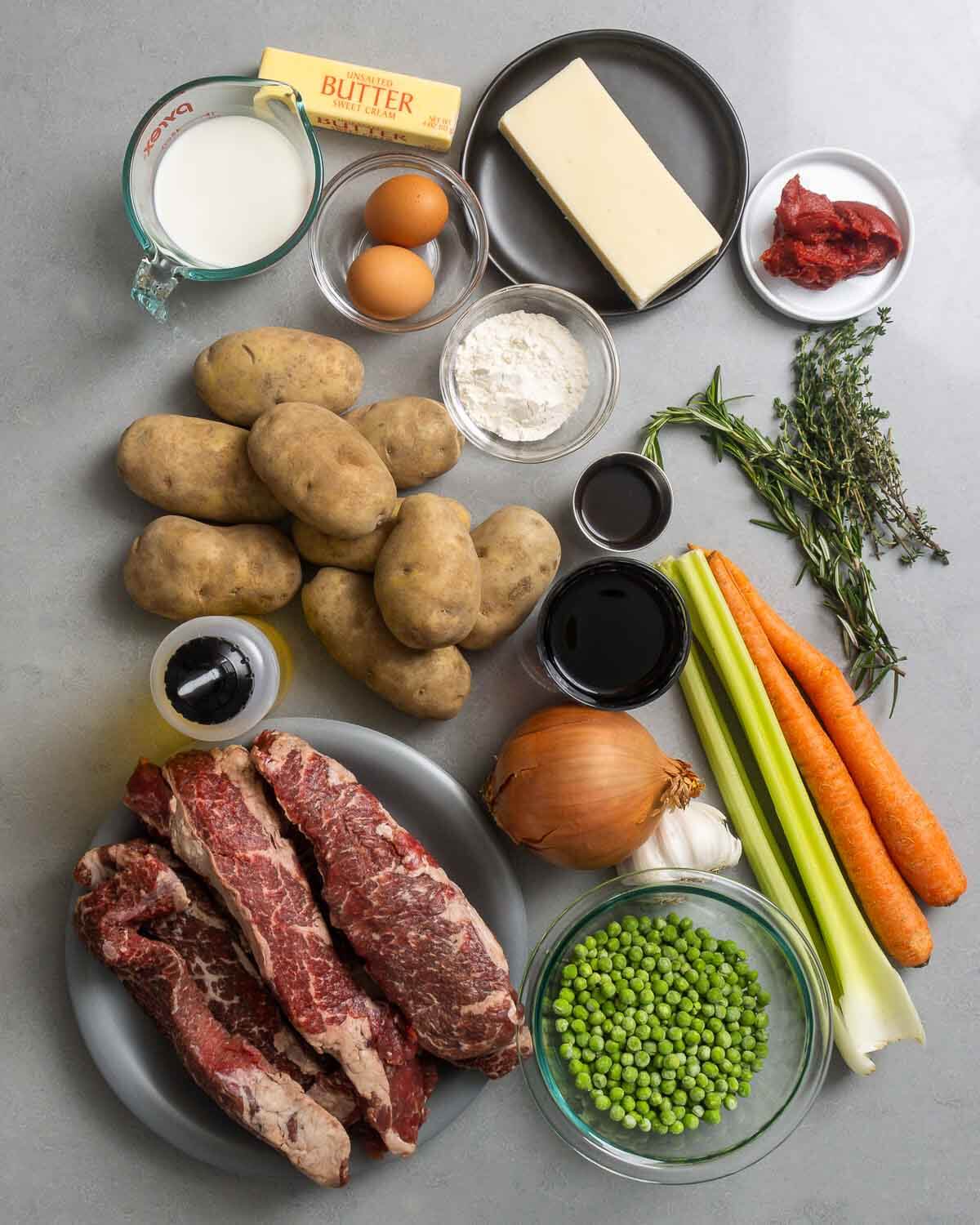 Ingredients shown: milk, butter, eggs, cheddar, tomato paste, flour, worcestershire sauce, herbs, potatoes, red wine, olive oil, celery, carrots, garlic, onion, peas, and boneless short ribs.