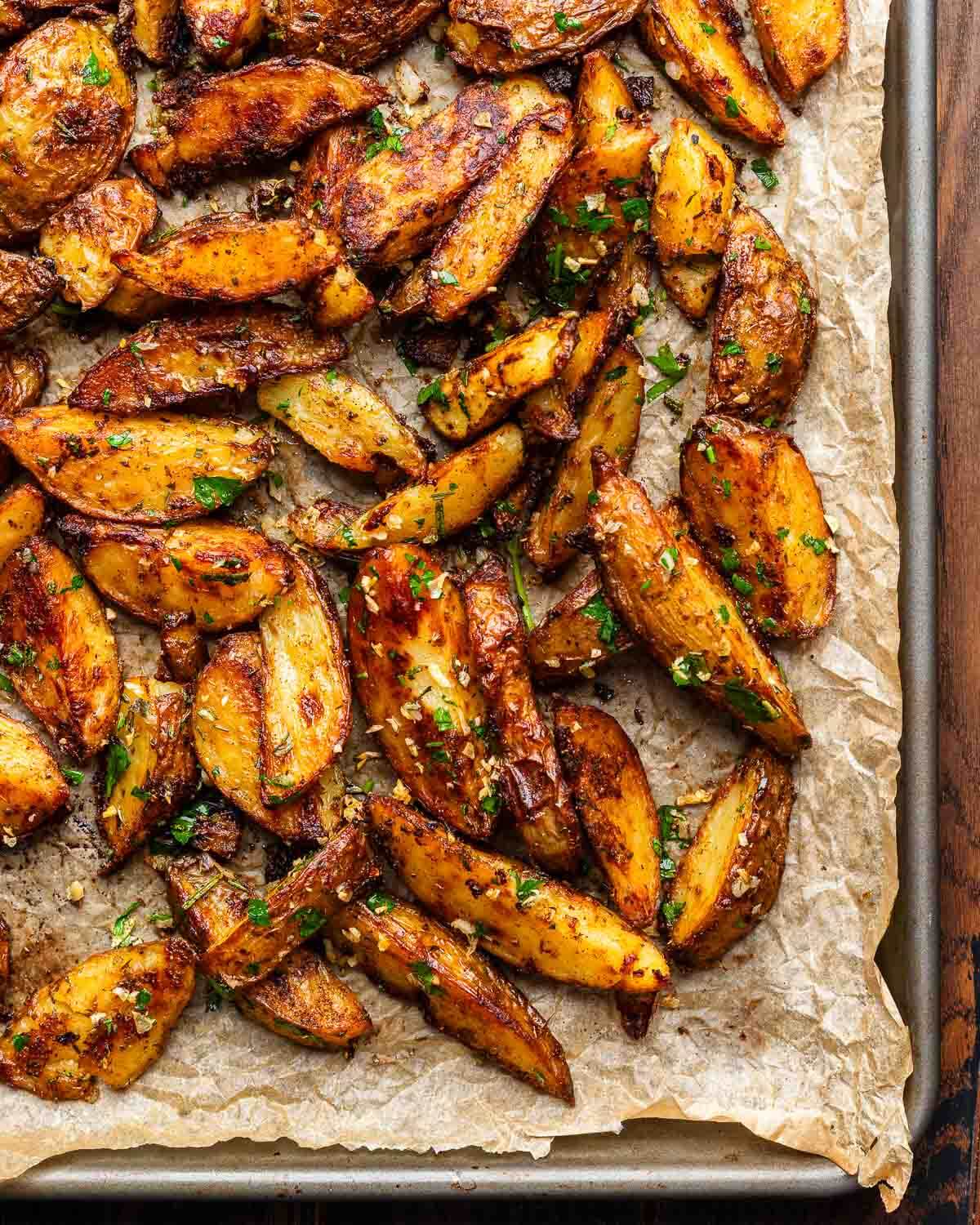 Cripsy roasted potatoes topped with garlic and herbs on brown parchment paper.