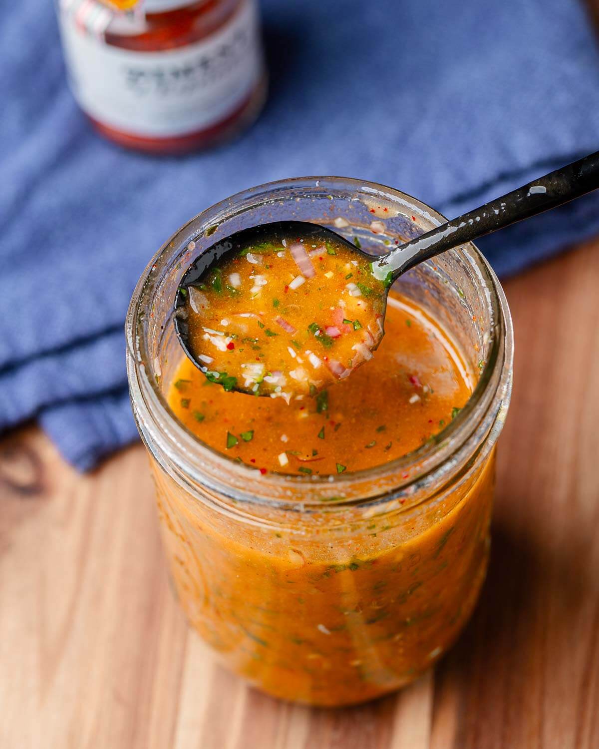 Pouring spoonful of dressing over mason jar.