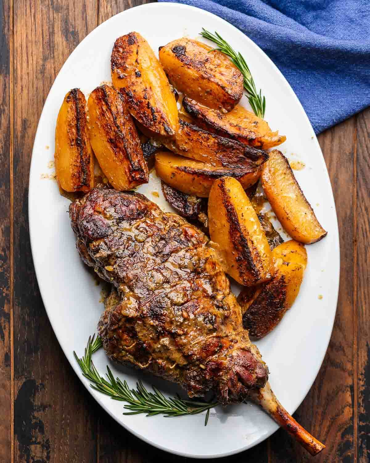 Large white platter with Greek-style bone-in leg of lamb and potatoes.